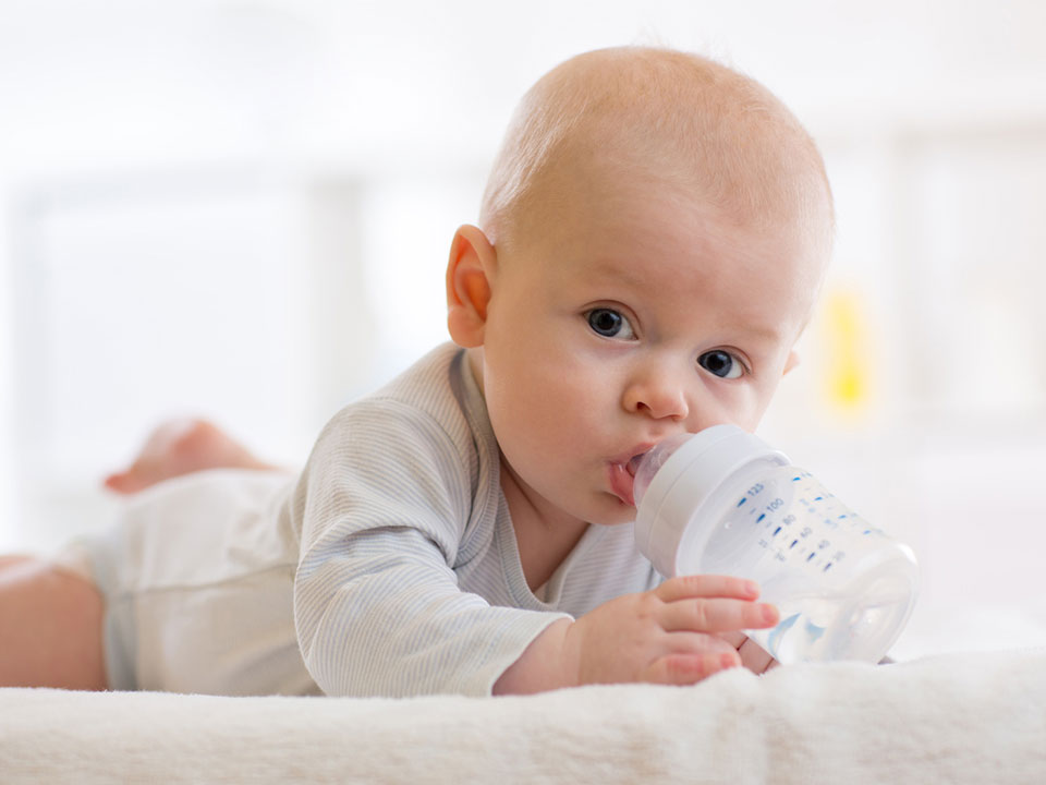 Baby liegt auf dem Bauch und trinkt Wasser aus einer Flasche